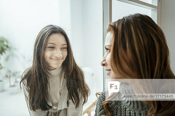Smiling girl looking at mother through window at home