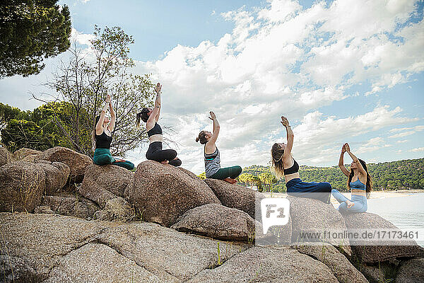 Junge Frauen mit Lehrerin üben Yoga auf einem Felsen
