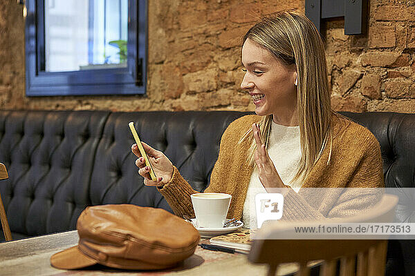 Smiling woman doing video call through smart phone while sitting in cafeteria