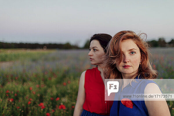 Mid adult woman standing with female friend in poppy field against sky