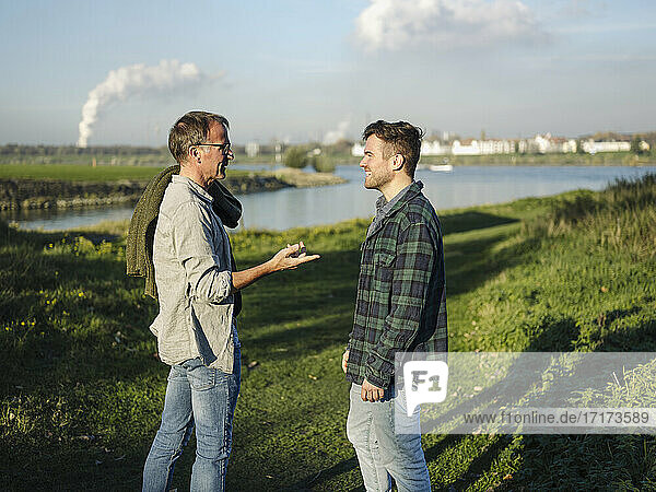 Father talking with son while standing on grass at riverbank