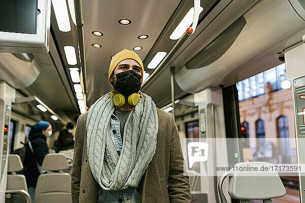 Mann mit Gesichtsschutzmaske  der im Zug stehend wegschaut