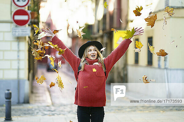 Carefree young woman throwing dry leaf while standing on street