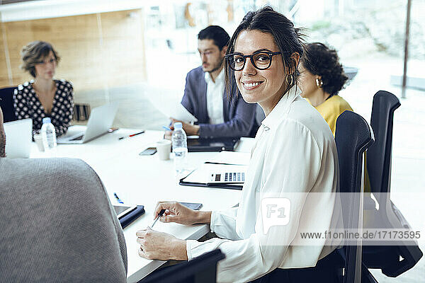 Smiling businesswoman sitting by colleagues in board room at coworking place
