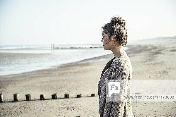 Young woman contemplating while standing on beach during sunny day