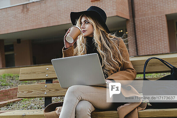 Woman with laptop drinking coffee while looking away