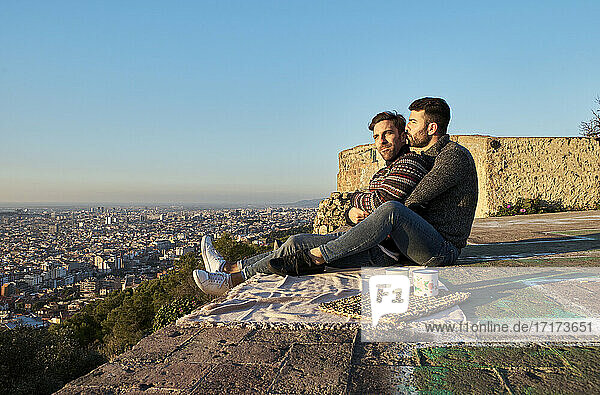 Romantic gay couple sitting on observation point against clear sky  Bunkers del Carmel  Barcelona  Spain