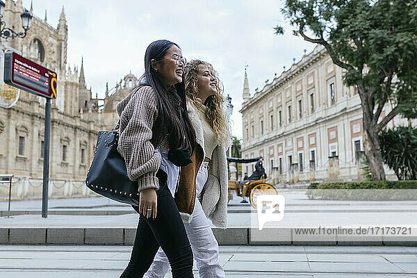 Multi-ethnic female friends walking on sidewalk in city