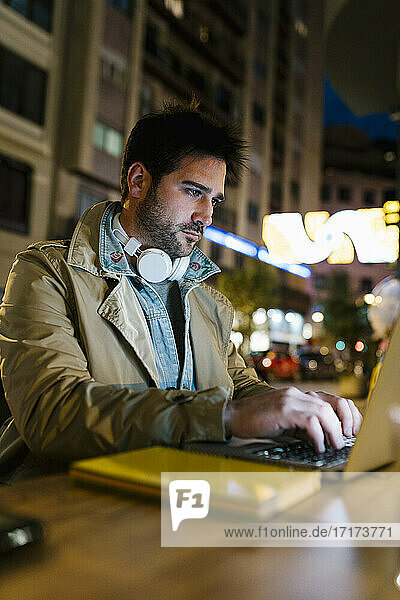 Mittlerer erwachsener Mann mit Kopfhörern  der einen Laptop benutzt  während er in einem Straßencafé sitzt