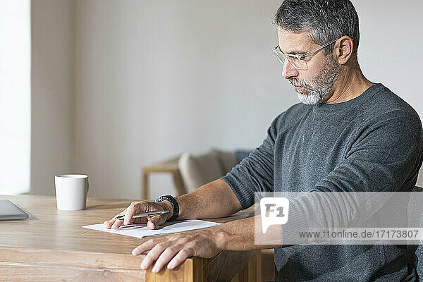 Älterer Geschäftsmann mit Brille  der bei der Arbeit im Büro zu Hause Papier liest