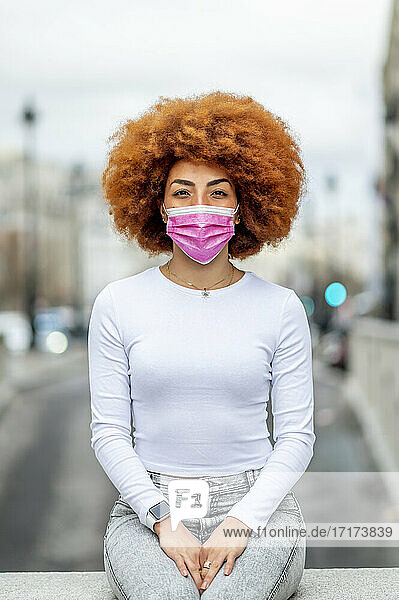 Mid adult woman wearing protective face mask while sitting on retaining wall