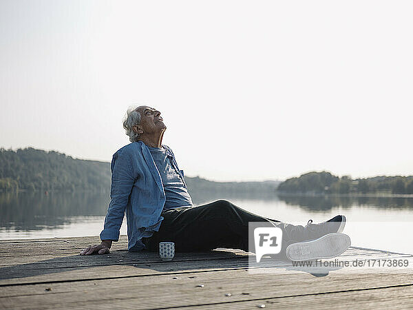 Unbeschwerter Mann  der sich auf dem Pier sitzend entspannt