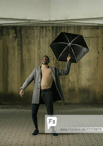 Young man with umbrella looking up while standing on footpath