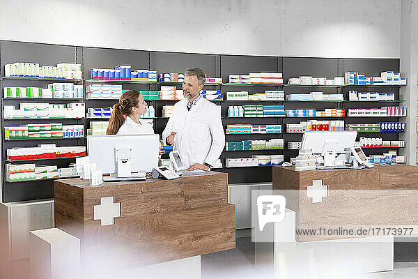 Female pharmacist with male colleague talking at pharmacy counter