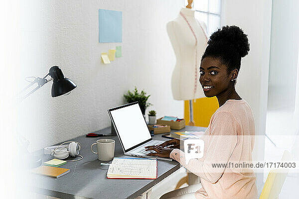 Lächelnde Modedesignerin  die im Büro zu Hause sitzt und einen Laptop benutzt