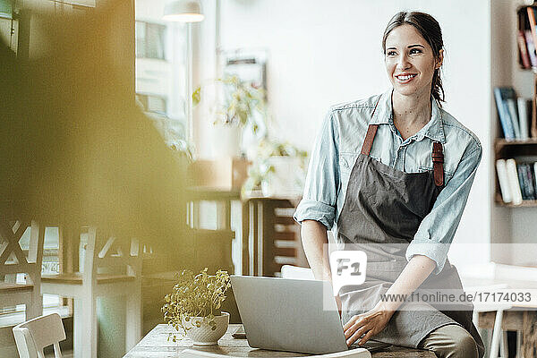 Smiling female owner with laptop at table in coffee shop