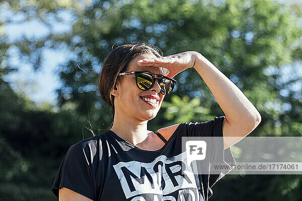 Nahaufnahme einer schönen Frau mit Sonnenbrille  die ihre Augen gegen Bäume im Park abschirmt