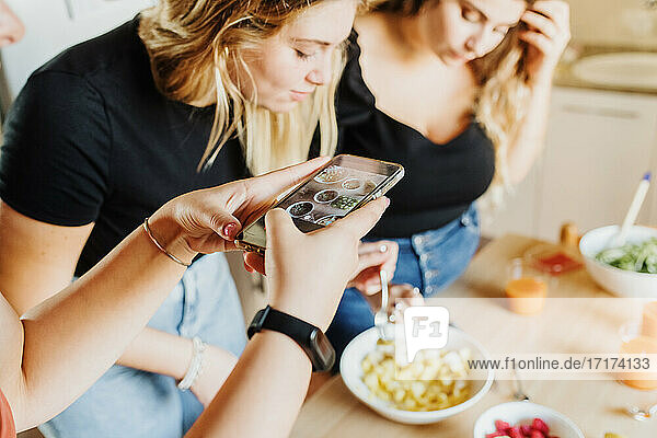Frau fotografiert mit dem Handy  während Freunde Eigentum freigegeben (PR) Essen zubereiten