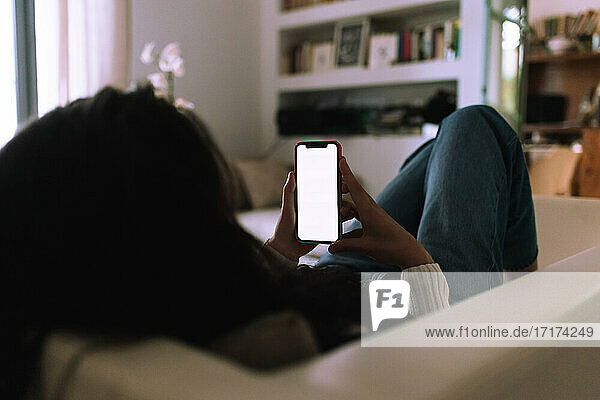 Junge Frau auf dem Sofa  schaut auf ihr Mobiltelefon