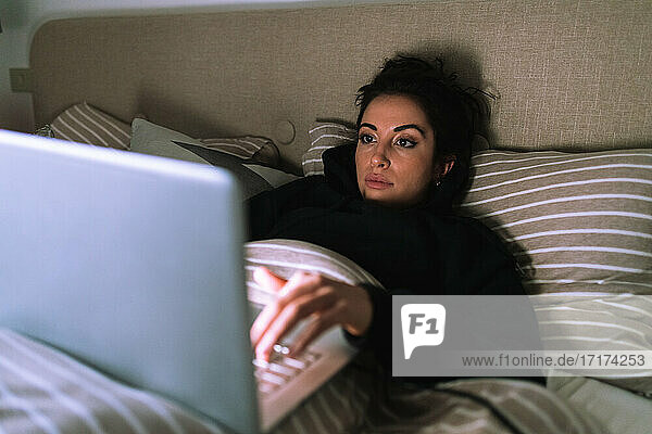Junge Frau arbeitet am Laptop im Bett