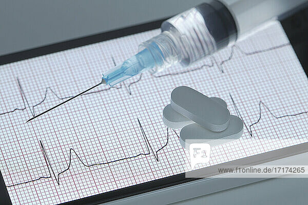 Pillen und eine Spritze auf dem Bildschirm eines Smartphones  das ein gesundes Elektrokardiogramm anzeigt