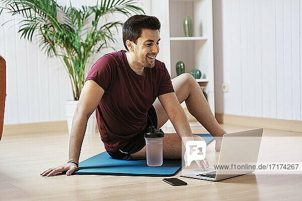 Man on exercise mat at home  using laptop