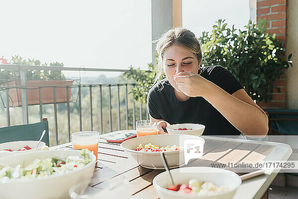 Junge Frau isst eine Mahlzeit auf dem Balkon