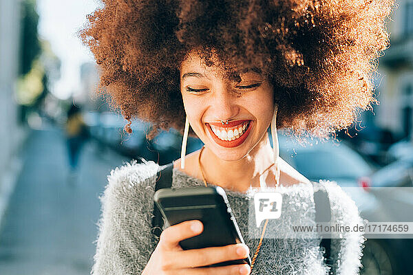 Junge Frau schaut lächelnd auf ihr Telefon im Freien