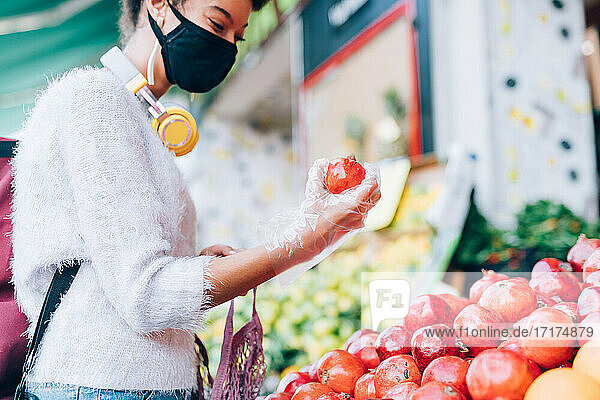 Junge Frau mit Gesichtsmaske und Handschuhen  die an einem Stand Obst auswählt