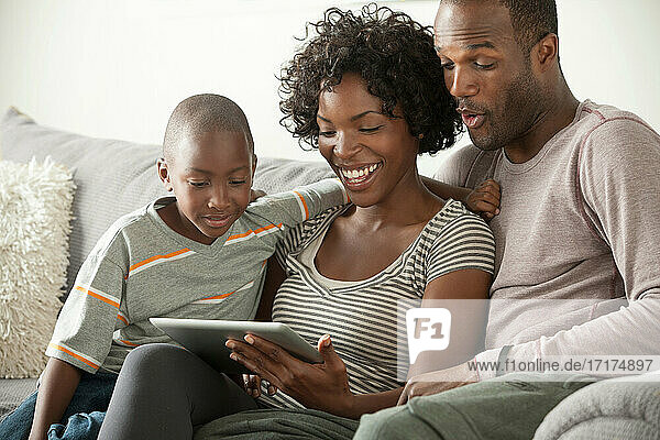 Boy with parents on sofa using digital tablet