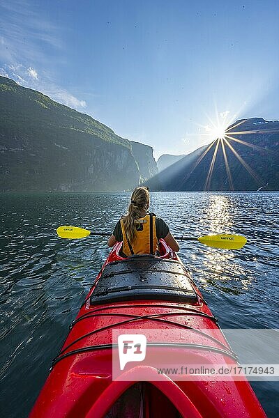 Junge Frau paddelt in einem Kajak  Sonne scheint  Geirangerfjord  bei Geiranger  Norwegen  Europa