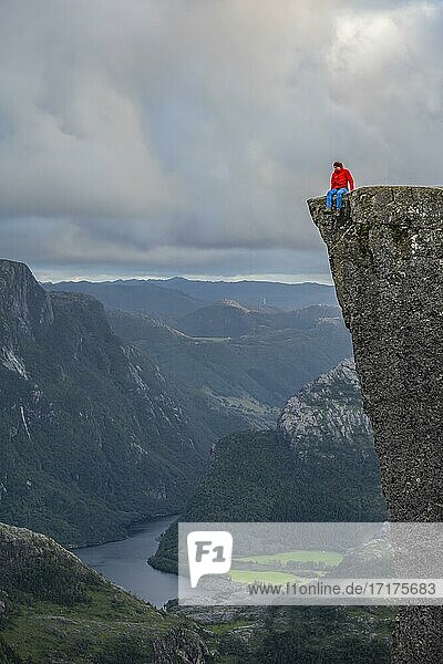 Einzelner Mensch sitzt auf der Kante am Felsplateau  Felskanzel Preikestolen  Lysefjord  Ryfylke  Rogaland  Norwegen  Europa
