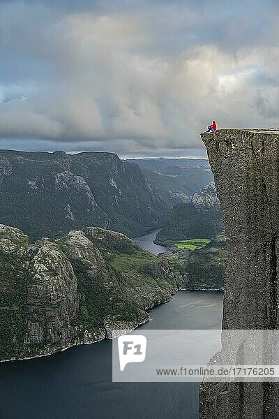 Einzelner Mensch sitzt auf Felsplateau  Felskanzel Preikestolen  Lysefjord  Ryfylke  Rogaland  Norwegen  Europa