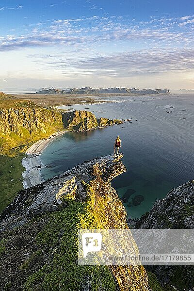 Abendstimmung  Wanderin steht am Abgrund auf Felsvorsprung  Blick auf Felsen  Strand und Meer  Gipfel des Berges Måtinden  bei Stave  Nordland  Norwegen  Europa