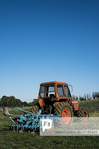 Red tractor with blue harrow on a farm.