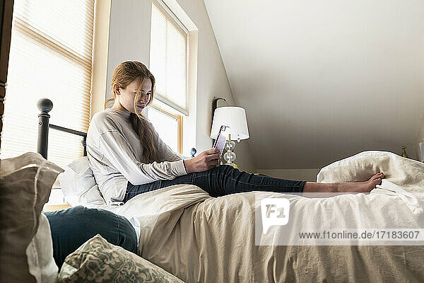 Teenager-Mädchen sitzt auf ihrem Bett und benutzt ihr Smartphone