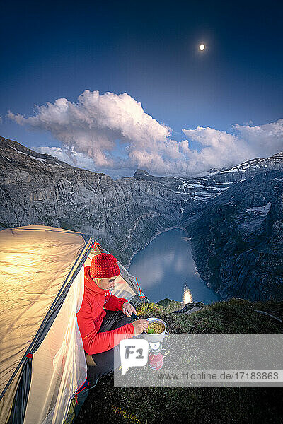 Hiker man cooking while camping in a tent above lake Limmernsee  Canton of Glarus  Switzerland  Europe
