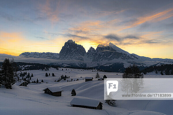 Mit Schnee bedeckte Berghütten mit Langkofel und Langkofel im Hintergrund in der Morgendämmerung  Seiser Alm  Dolomiten  Südtirol  Italien  Europa