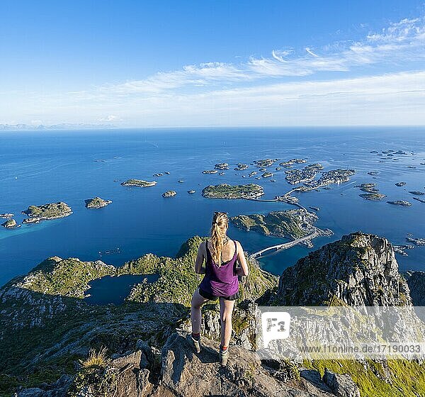 See Heiavatnet  Häuser auf kleinen Felsinseln im Meer  Wanderin blickt vom Gipfel des Berges Festvågtind auf Henningsvær  Vågan  Lofoten  Nordland  Norwegen  Europa