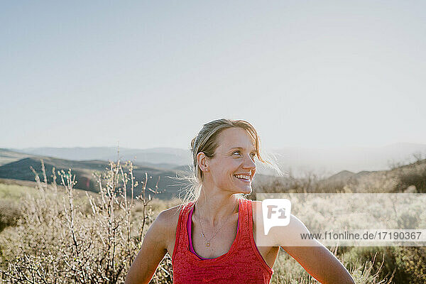 Athletic blonde woman laughs with sun and mountains behind her