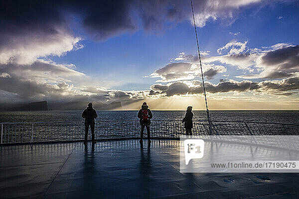 Drei Personen genießen den Sonnenuntergang auf dem Bootsdeck  während das Schiff nach Island fährt