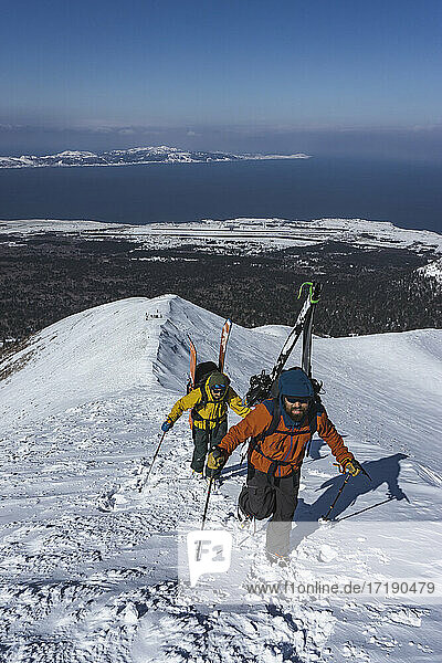 Menschen mit Skistöcken beim Klettern auf einen schneebedeckten Berg im Urlaub