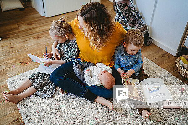 Weiße Mutter  die ihre Kinder umarmt und Bücher liest  während sie zu Hause auf dem Teppich sitzt