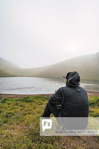Unbekannter Mann vor einem Vulkansee sitzend und um sich blickend