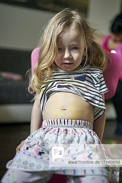 Nettes kleines Mädchen  das auf einem Stuhl sitzt und ihren schmerzenden Bauch zeigt.