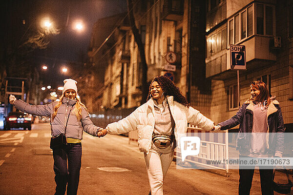 Glückliche Freundinnen  die sich an den Händen halten  gehen nachts auf der Straße in der Stadt