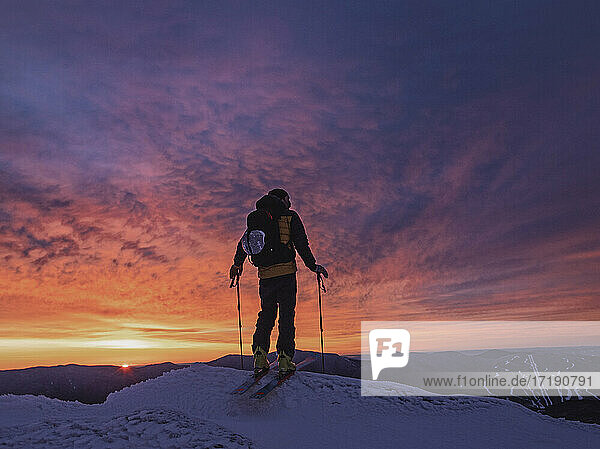 Skier silhouetted against red sunrise on mountain peak  New Hampshire