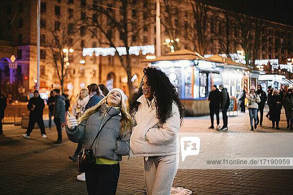 Glückliche weibliche Freunde gehen auf der Straße in der Stadt bei Nacht im Winter