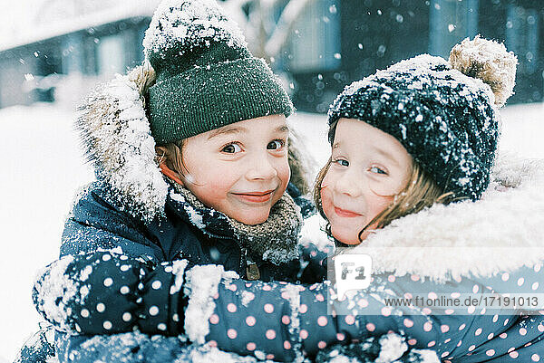 Two children hugging in snow and playing together in nor'easter storm