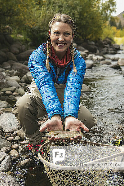 Portrait of smiling young woman with fish catch at stream in forest